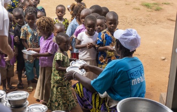 An adult handing bowls to a queue of children