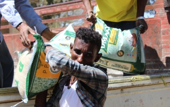 A man walking away from a truck with a large food sack on his shoulder