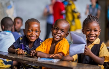 Three children sit at a desk smiling at the camera