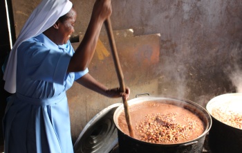 A Sister stirring a large pot full of steaming hot food