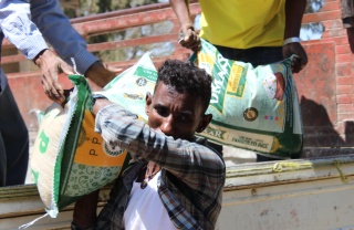 A man walking away from a truck with a large food sack on his shoulder