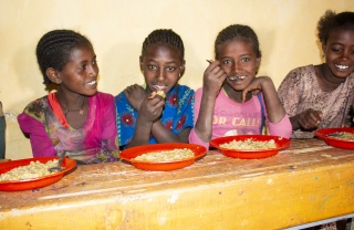 Four young girls sitting at a bench in front of food bowls smiling and looking happy.