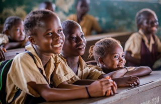 Three children sit in a row at a desk facing ahead and smiling