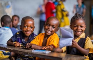 Three children sit at a desk smiling at the camera