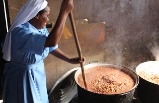 A Sister stirring a large pot full of steaming hot food