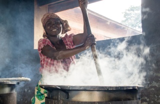 woman stirring a huge steaming cauldron smiling at camera