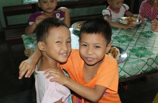 Two young boys with arms around each other smiling happily at the camera
