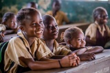 Three children sit in a row at a desk facing ahead and smiling