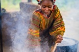 A woman facing the camera leans over and stirs a large steaming pot