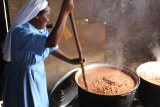 A Sister stirring a large pot full of steaming hot food