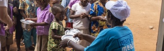 An adult handing bowls to a queue of children