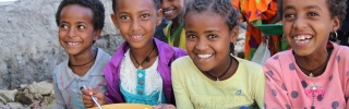 Four children sit next to each other smiling and holding almost empty bowls of rice