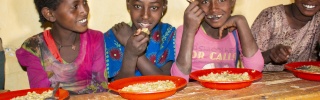 Four young girls sitting at a bench in front of food bowls smiling and looking happy.