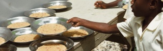 A child taking a bowl of rice off a table.