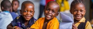 Three children sit at a desk smiling at the camera