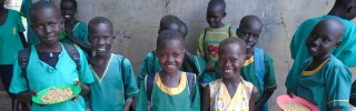 Line of children holding bowls of food smiling at camera