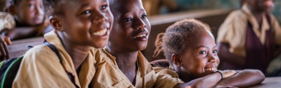 Three children sit in a row at a desk facing ahead and smiling