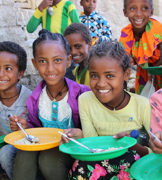 Four children sit next to each other smiling and holding almost empty bowls of rice