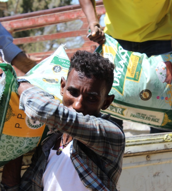 A man walking away from a truck with a large food sack on his shoulder