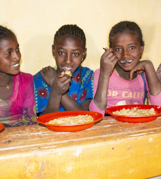 Four young girls sitting at a bench in front of food bowls smiling and looking happy.