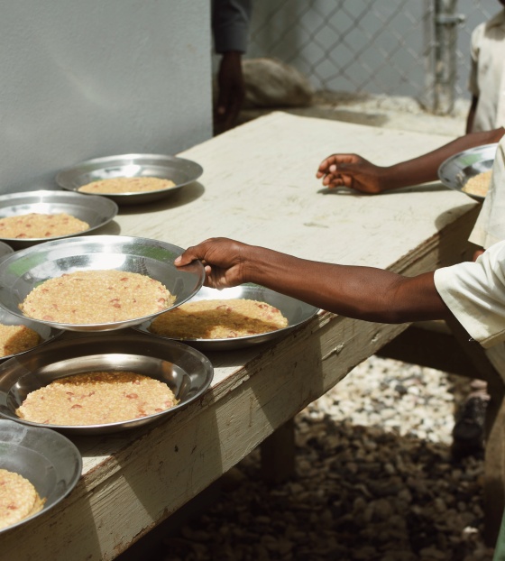 A child taking a bowl of rice off a table.