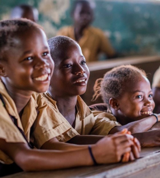 Three children sit in a row at a desk facing ahead and smiling