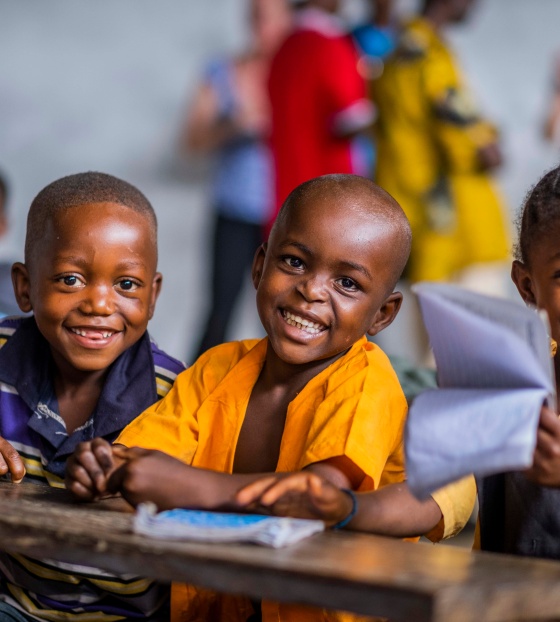 Three children sit at a desk smiling at the camera