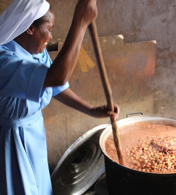 A Sister stirring a large pot full of steaming hot food