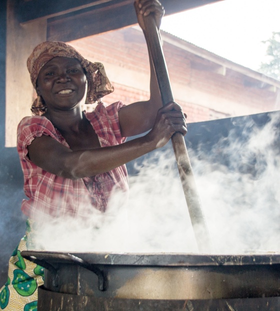 woman stirring a huge steaming cauldron smiling at camera