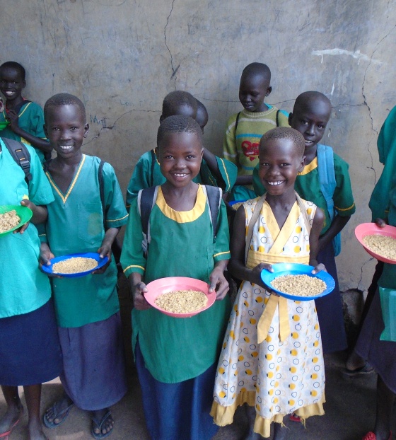 Line of children holding bowls of food smiling at camera