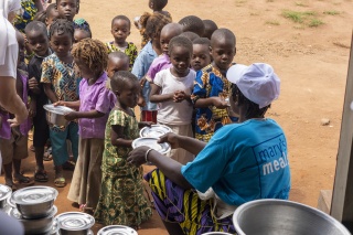 An adult handing bowls to a queue of children