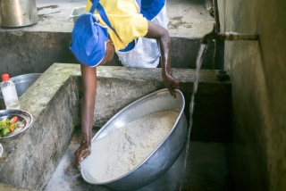 An adult leaning over a sink, washing a large bowl of rice