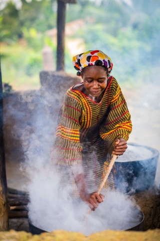 A woman facing the camera leans over and stirs a large steaming pot