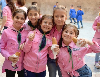 A group of five children in pink shirts hold up sandwiches and smile at the camera